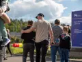 Rodzina idzie w stronę aresztu. Dzieci trzymają się za ręce, a dorośli obejmują się nawzajem. W tle widać ogrodzenie i tablicę informacyjną. To obraz matki za kratami, która spotyka się z bliskimi.