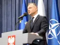 Prezydent Andrzej Duda przemawia przy mównicy z godłem Polski. Za nim flagi UE i NATO. Może to być związane z ułaskawieniem prezydenta.