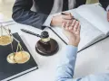 Prawnik pomaga klientowi wypełnić wniosek o zamianę kary pozbawienia wolności na pracę społeczną. Na stole waga sprawiedliwości i młotek sędziowski.