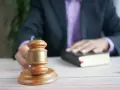 Sędzia kładzie rękę na księdze, obok młotka. Czas oczekiwania na uprawomocnienie wyroku karnego może być różny.