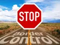 Droga prowadzi przez pustynny krajobraz, a na niej znak STOP i napis "Border Control". To symbol zakazu opuszczania kraju.