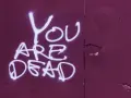 Napis "YOU ARE DEAD" białą farbą na fioletowej ścianie. Groźba jak z artykułu 190 paragraf 1 kk.