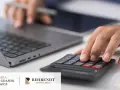 Dłoń na kalkulatorze, obok laptopa. Specjaliści pomagają w postępowaniu karno skarbowym.