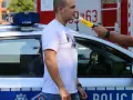 Policjant przeprowadza procedurę badania alkomatem. Mężczyzna dmucha w urządzenie przy radiowozie.