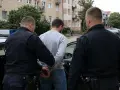 Policjanci w kajdankach prowadzą mężczyznę do radiowozu. To może być efekt zatrzymania telefonu przez prokuratora w związku ze śledztwem.