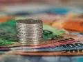 Stos monet na kolorowych banknotach. W tle widoczne fragmenty banknotów o nominałach 100 i 200, co może nawiązywać do artykułu 278 kpk.