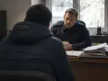 Policjant w mundurze rozmawia z mężczyzną w kurtce. Na biurku stosy dokumentów, jakby przygotowywano komentarz do art. 284 par. 2 kk.