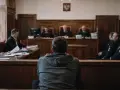 Młody mężczyzna w szarej bluzie siedzi tyłem do widza, w sali sądowej. Jest małym świadkiem koronnym, otoczonym przez sędziów i policjantów.
