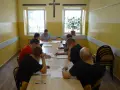 Grupa mężczyzn uczestniczy w zajęciach, które mogą być częścią system programowanego oddziaływania. Siedzą przy stole, studiując dokumenty.