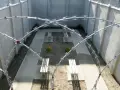 Pusty spacerniak w więzieniu z ławkami i kilkoma kwiatami, otoczony betonowymi murami i drutem kolczastym.