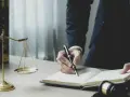 Prawnik pisze notatki do sprawy, obok wagi sprawiedliwości i ksiąg prawnych.