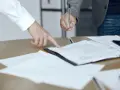 Dwie osoby przy biurku analizują dokumenty. Jedna wskazuje palcem na tekst, druga trzyma długopis, gotowa do podpisania. To może być moment, gdy omawiają, co to jest list żelazny.
