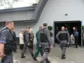 Strażnicy więzienni eskortują więźnia na pogrzeb. Widać ich w mundurach przed budynkiem, gdzie odbywa się ceremonia.