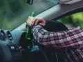 Mężczyzna w kratę, z butelką w ręku, opiera się o kierownicę. Pytanie: po ilu latach występuje przedawnienie za jazdę pod wpływem alkoholu?