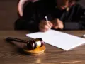 Młotek sędziowski na drewnianym stole, w tle osoba pisząca dokument. Symbol sprawiedliwości i wyrok łączny po nowelizacji.