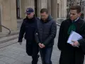 Policjant eskortuje podejrzanego przed budynkiem sądu. Ile jest więzień w Polsce? To pytanie nurtuje wielu.