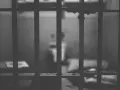 Widok przez kraty więzienne. Ciemne, ponure wnętrze celi, symbolizujące karę pozbawienia wolności.