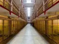 Korytarz więzienny z celami po obu stronach. W oddali widać grupę zwiedzających. To miejsce, gdzie kiedyś przebywali więźniowie, teraz jest atrakcją turystyczną, jak np. w bloku 217c kkw.