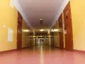 Długi korytarz z rzędem drzwi, typowy dla zakładu karnego dla kobiet. Jasne ściany i drzwi z numerami cel.