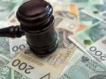 Młotek sędziowski na stosie polskich banknotów. Określenie "stawka dzienna kk" może sugerować koszty sądowe lub kary finansowe.