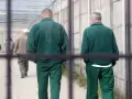 Dwóch mężczyzn w zielonych strojach więziennych w Polsce idzie korytarzem.