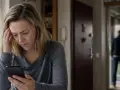 Zmartwiona kobieta z telefonem w dłoni, czuje niepokój, gdy ktoś wchodzi do domu.