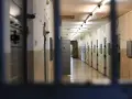 Korytarz więzienny z rzędami cel po obu stronach, widok przez kraty.