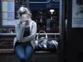 Dziewczyna na przystanku nocnego autobusu, pochłonięta telefonem, ignoruje uporczywe niepokojenie. Obok torba.