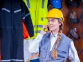 Kobieta w żółtym kasku rozmawia przez telefon, otoczona odzieżą roboczą. Może to być związane z artykułem 220 kodeksu karnego, dotyczącym bezpieczeństwa pracy.