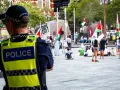 Policjant w kamizelce odblaskowej obserwuje tłum z flagami. Sytuacja przypomina zatrzymanie nieletniego przez policję, choć nie widać konkretnego zdarzenia.