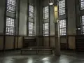 Wnętrze przypominające zakład karny typu otwartego w Polsce. Widać kraty w oknach, ławki i regały.