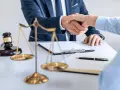 Uścisk dłoni prawników przy biurku z wagą sprawiedliwości i młotkiem. Sprawa 157 kk zakończona sukcesem.