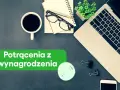 Biurko z laptopem, kawą i notatnikiem. Zielony baner informuje o potrąceniach z wynagrodzenia skazanego.