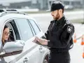 Policjant spisuje dane kierowcy, który może być zagrożony **przepadkiem pojazdu**. Kobieta w okularach siedzi za kierownicą białego samochodu.