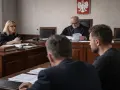 W sali sądowej trwa posiedzenie aresztowe. Sędzia w todze przegląda dokumenty, obok siedzi prokuratorka, a przed nimi mężczyźni w garniturach.