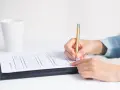 Dłoń pisze złotym długopisem na formularzu, przygotowując wniosek o zatarcie skazania.