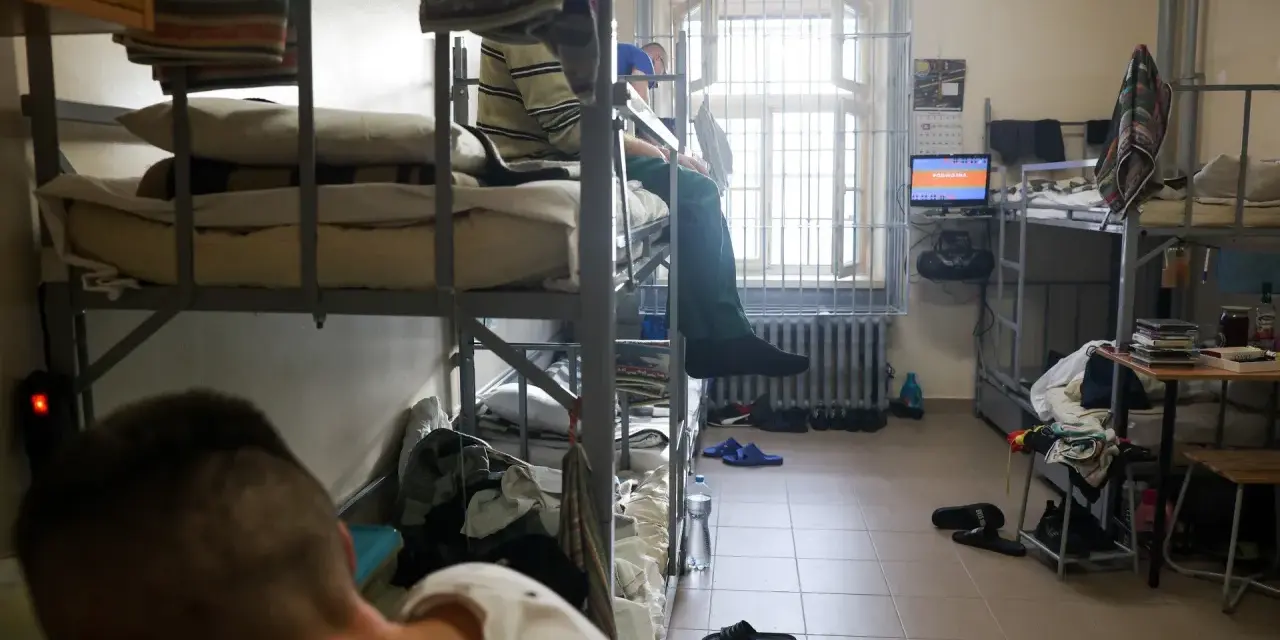 Wnętrze celi, areszt śledczy. Dwie osoby na łóżkach piętrowych, okno z kratami, telewizor.