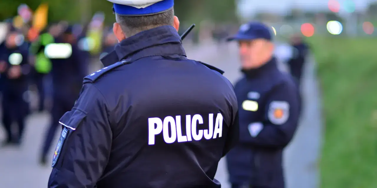 Policjanci w mundurach, jeden z napisem "POLICJA" na plecach, gotowi do akcji. Czy to kontrola osobista, czy przeszukanie?