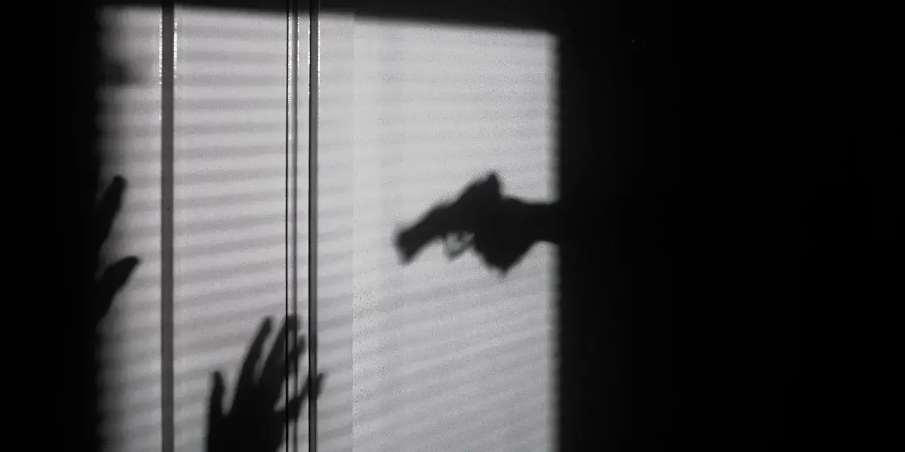 Cień dłoni z pistoletem grozi dwóm dłoniom, które próbują się zasłonić. To scena jak z filmu o świadku koronnym.
