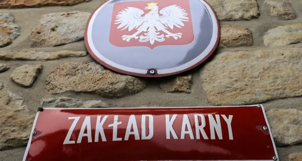 Tablica z napisem "ZAKŁAD KARNY" i godło Polski na kamiennej ścianie.
