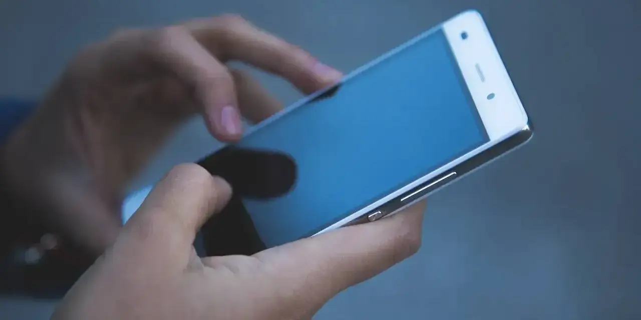 Dłonie trzymają biały smartfon. Czy na dołku można mieć telefon? Tak, nawet w trudnych chwilach można pozostać w kontakcie.