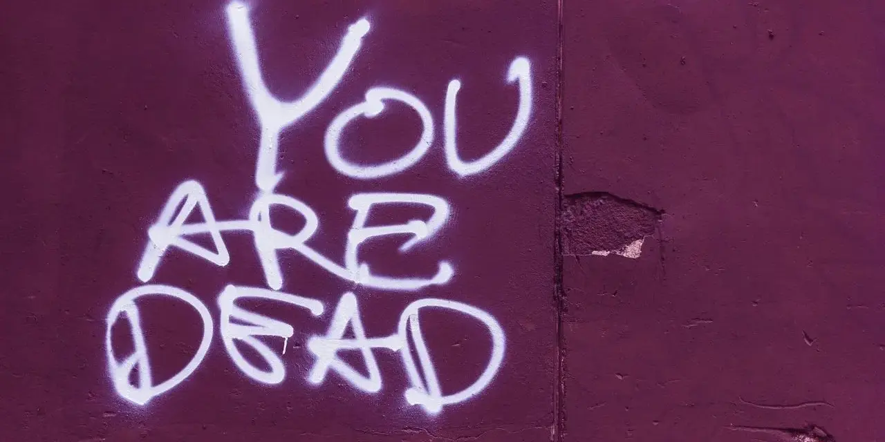 Napis "YOU ARE DEAD" białą farbą na fioletowej ścianie. Groźba jak z artykułu 190 paragraf 1 kk.