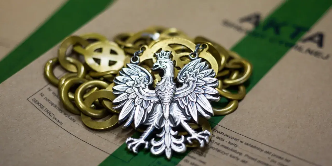 Srebrny orzeł na złotym łańcuchu, leżący na aktach. Symbolizuje prekluzja dowodowa w polskim prawie.
