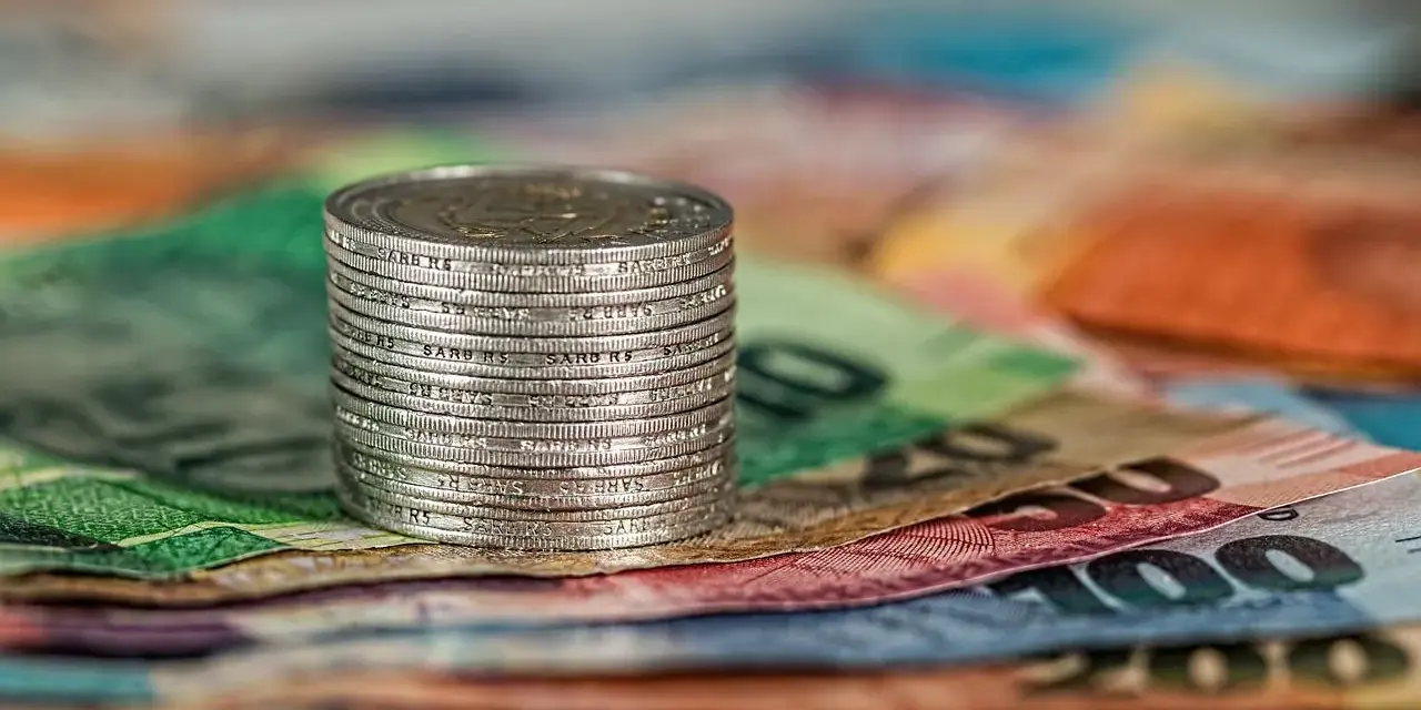 Stos monet na kolorowych banknotach. W tle widoczne fragmenty banknotów o nominałach 100 i 200, co może nawiązywać do artykułu 278 kpk.