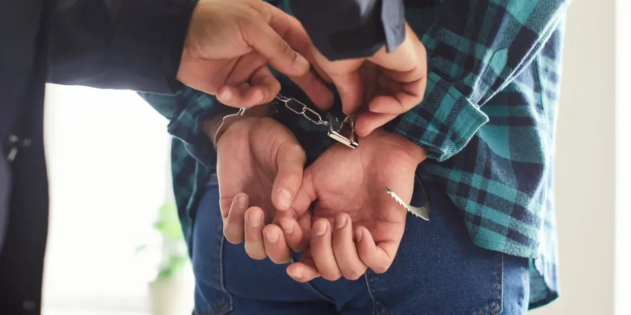Policjant zakłada kajdanki podejrzanemu o narkotyki. Kaucja za wyjście z aresztu za narkotyki jest zmienna.