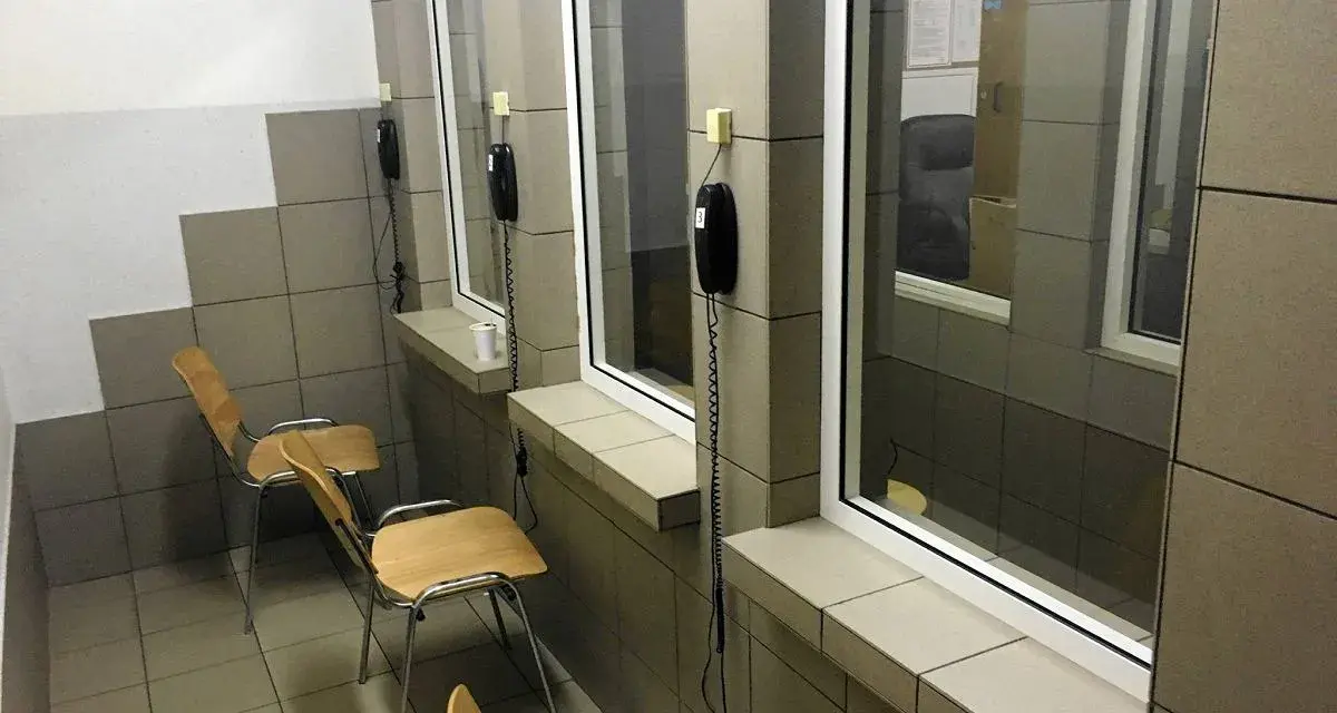 Pokój widzeń w zakładzie karnym półotwartym. Proste krzesła i telefony czekają na rozmowy.