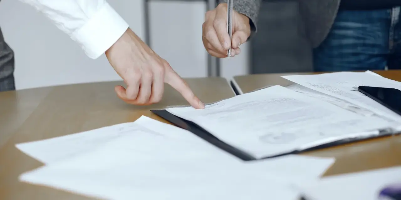 Dwie osoby przy biurku analizują dokumenty. Jedna wskazuje palcem na tekst, druga trzyma długopis, gotowa do podpisania. To może być moment, gdy omawiają, co to jest list żelazny.