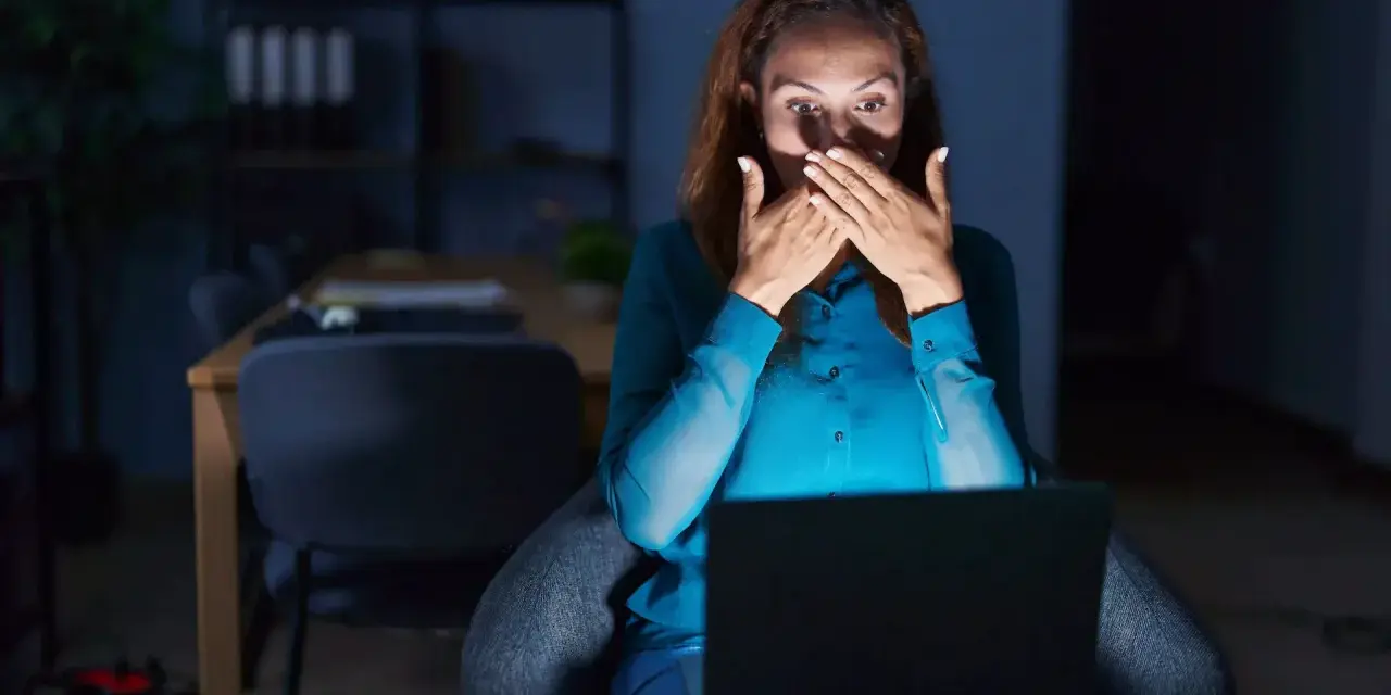 Kobieta zszokowana treścią na laptopie, czuje się jakby była obiektem prześladowania kogoś.