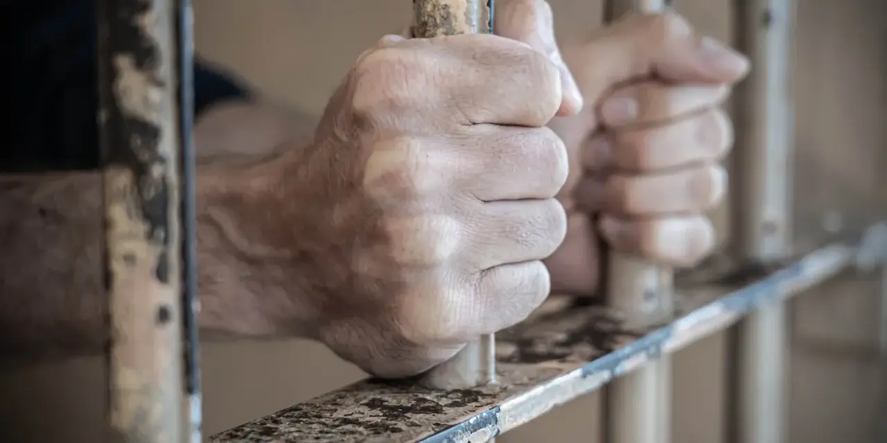Dłonie więźnia zaciskają się na kratach. Może to być symbol nadziei na zwolnienie, gdy przygotowuje wniosek do dyrektora zakładu karnego wzór.