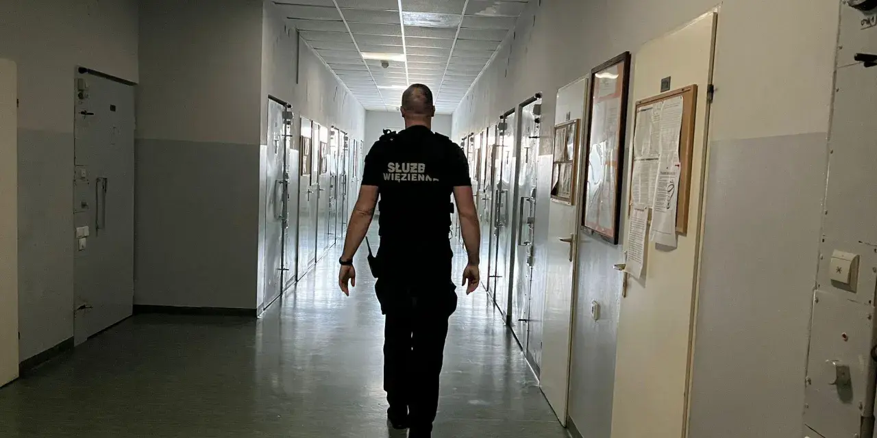 Strażnik więzienny idzie korytarzem, gdzie odbywa się klasyfikacja skazanych. Wzdłuż korytarza znajdują się cele.